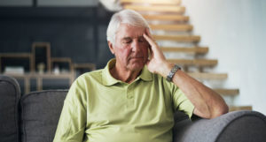 elderly man clasps his temple in distress