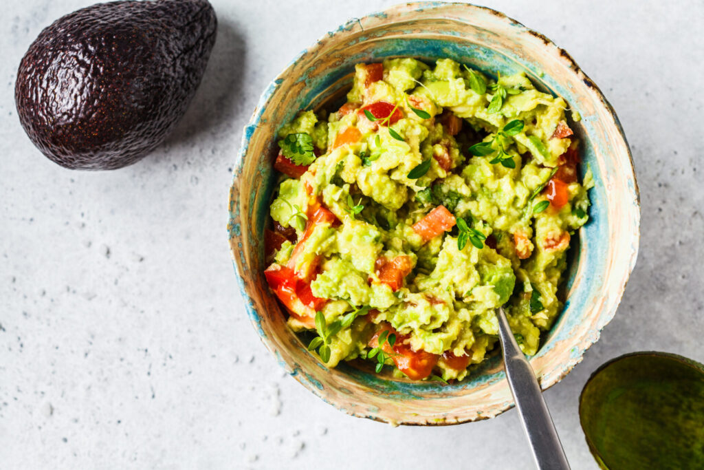 Fresh avocado tomato guacamole in a bowl, top view. Healthy vegan food concept.