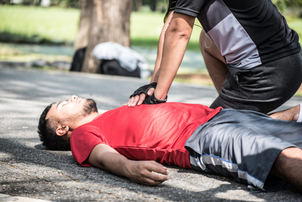 Unconscious man lying on the ground. His friend is kneeling over him and performing CPR.