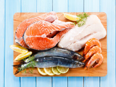 Cuts of fish and seafood, including salmon, cod, and shrimp, all staged together on a cutting board