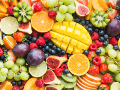 Assortment of healthy raw fruits and berries platter background, strawberries raspberries oranges plums apples kiwis grapes blueberries, mango, and others.