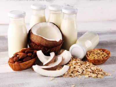 Jars of dairy and dairy-free milk with coconuts, oats, almonds, and soybeans surrounding the jars