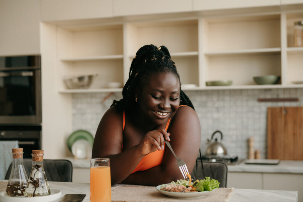 African-American woman in her kitchen wearing athletic clothing and eating a plate of veggies