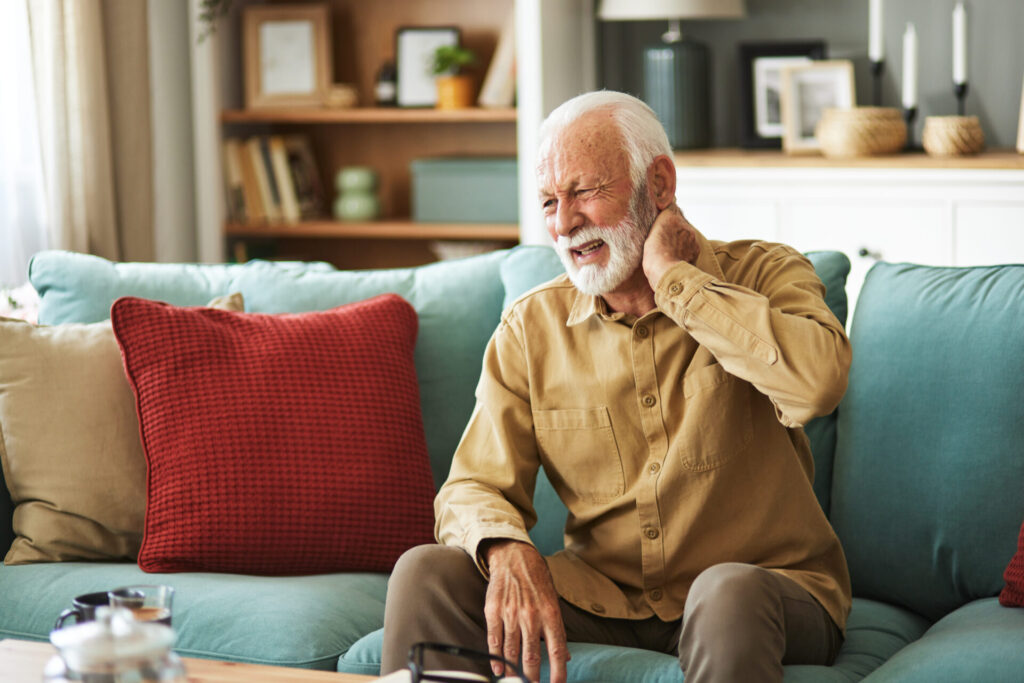 Older man sitting on his couch clutching his neck in pain